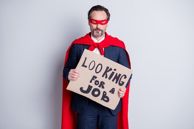 Zdjęcie szukać pracy. zdjęcie zestresowany dojrzały odrzucony biznesowy facet super bohater kostium przytrzymaj afisz potrzeba pracy poproś o pomoc nosić garnitur czerwony maska na twarz płaszcz na białym tle szary tło