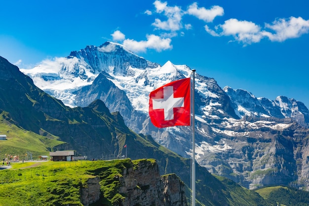 Szwajcarska flaga macha i turyści podziwiają szczyty góry Jungfrau na punkt widokowy Mannlichen, Berneński Oberland Szwajcaria