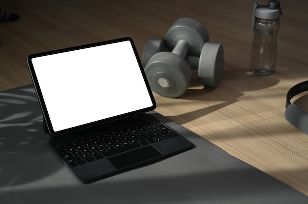 Tablet komputerowy, hantle i butelka wody na podłodze w salonie. Trening fitness online