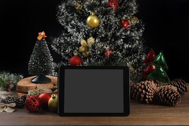 Tablet na czarnym tle z dekoracją świąteczną i drewnianym stołem.