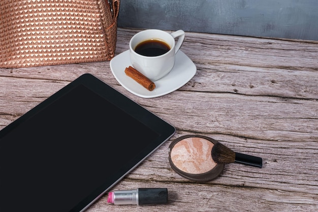 Tablet na stole otoczony filiżanką kawy w proszku i kosmetyczką w szmince