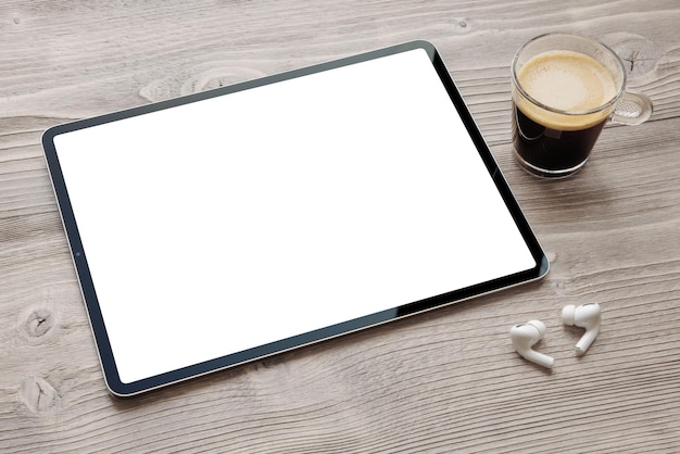 Zdjęcie tablet z pustym białym ekranem bezprzewodowymi słuchawkami i filiżanką kawy na drewnianym biurku