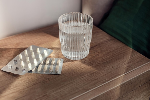 Tabletki kapsułki lekarstwo i szklanka wody na drewnianym tle