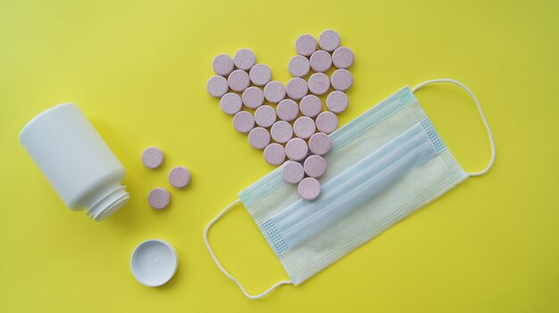 Zdjęcie tabletki lekarskie w kształcie różowego serca leżały płasko obok maski medycznej i białej butelki