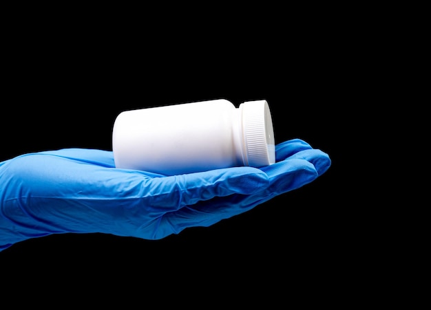 Tabletki medyczne w białym słoiku na odosobnionym czarnym tle z odbiciem w dłoni