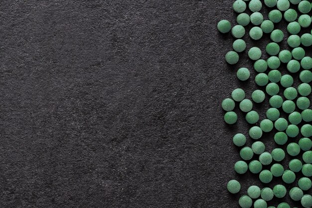 Tabletki Spirulina na czarnym tle. Zielone tabletki superfood. Płaski układanie, widok z góry, kopia przestrzeń