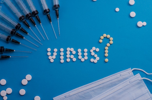 Zdjęcie tabletki ułożone ze słowem wirus ze znakiem zapytania i strzykawki na jasnoniebieskim tle. jakie są objawy wirusa? problemy dystrybucji i leczenia.