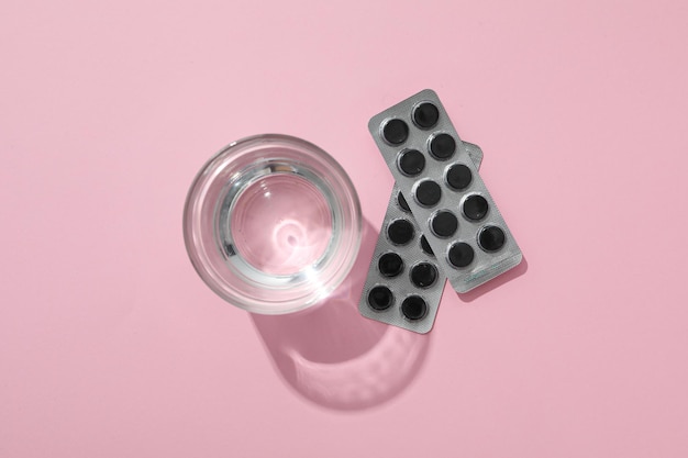 Tabletki węgla aktywnego i szklanka wody na różowym tle