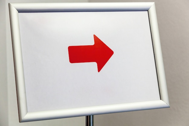 Zdjęcie tablica z białą ramką i czerwoną strzałką na stojaku.