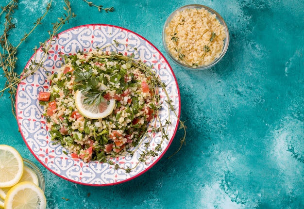 Tabule - orientalna sałatka, przystawka na niebieskim tle obok cytryny i bulguru.