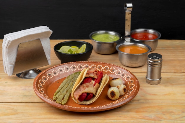 Taco z kiełbaskami na glinianym talerzu w towarzystwie cebulowych nopalów i salsy na drewnianym stole