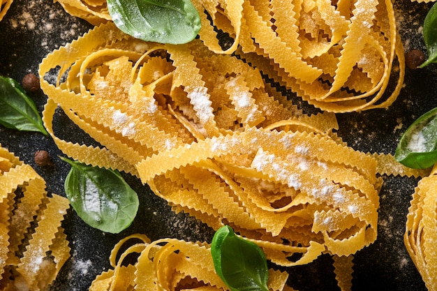 Tagliatelle. Domowy makaron, liście bazylii, mąka, papryka, oliwa z oliwek i pomidorek koktajlowy na ciemnym czarnym tle. Koncepcja żywności. Makieta. Poziomo z miejsca na kopię.