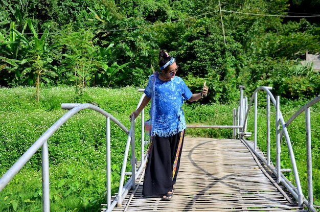 Tajska kobieta używa smartfona, aby zrobić zdjęcie wioski Baan Natong na drewnianym bambusowym moście w Phare Tajlandia