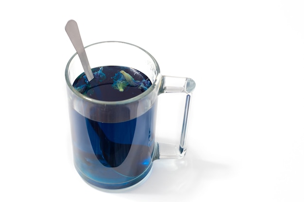 Tajska niebieska herbata w szklanym kubku i łyżce na białym tle odizolowane
