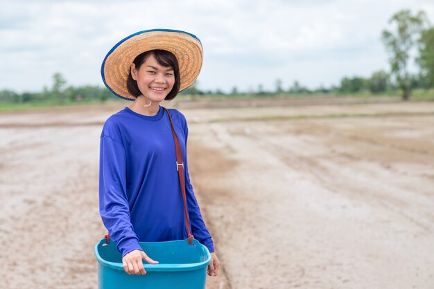 Tajski rolnik kobieta trzyma niebieskie wiadro zawiera stojących nasion ryżu i uśmiech na polu uprawy ryżu
