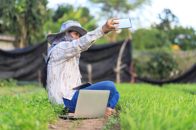 Tajski rolnik używający smartfona do robienia zdjęć selfie w uprawie warzyw w porannej chwale, w przypadku koncepcji rolnictwa ekologicznego i inteligentnego, wybierz ostrość, płytka głębia ostrości