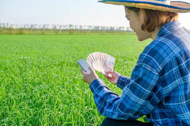 Tajskie banknoty z pustym ekranem smartfonu są przechowywane przez rolniczki na zielonych farmach