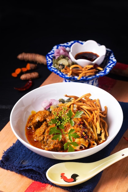 Tajskie jedzenie koncepcja Khao soi lub Khao soy tajska wołowina curry z makaronem jajecznym na drewnianej desce na czarnym tle z kopią miejsca