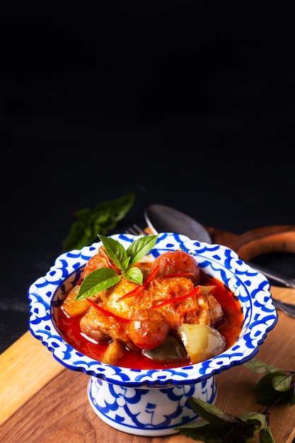 Zdjęcie tajskie jedzenie koncepcja pieczone czerwone curry z kurczaka na drewnianej desce na czarnym tle z miejscem na kopię