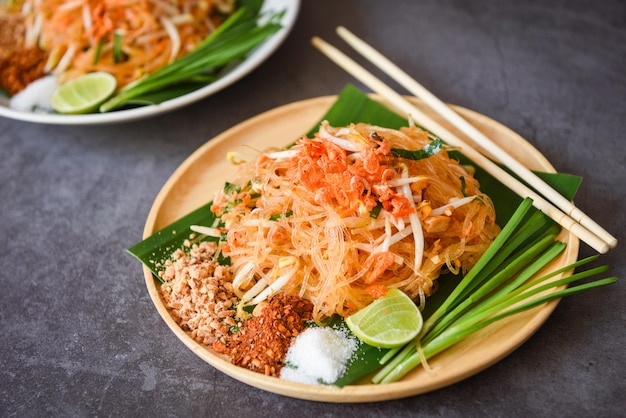 Tajskie jedzenie smażony makaron po tajsku z krewetkami kiełkami fasoli i orzeszkami ziemnymi chili proszek cukier cytryna limonka, smażony makaron Pad Thai na talerzu podawany na stole jedzenie - widok z góry