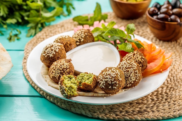 Talerz Falafel z dipem podawany w naczyniu odizolowanym na drewnianym stole widok z boku bliskowschodnich potraw