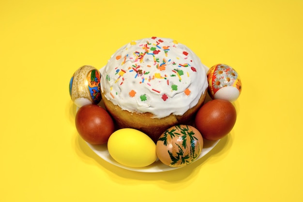 Talerz jajek i ciasto wielkanocne z wielokolorową posypką cukrową na żółtym tle