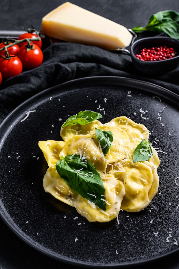 Zdjęcie talerz ravioli z parmezanem i bazylią. czarne tło. widok z góry