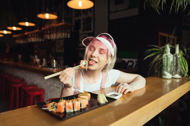 Zdjęcie talerz rolek sushi w restauracji z kobieta trzyma pałeczki