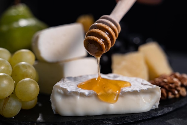 Talerz serów: Emmental, Camembert, Parmezan, ser pleśniowy, paluszki chlebowe, orzechy włoskie, orzechy laskowe, miód, winogrona. Czarne tło, zbliżenie.