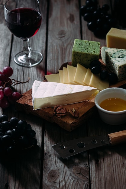 Talerz serów na ciemnym tle. Brie, dor blue, gouda, winogrona, orzechy, wino