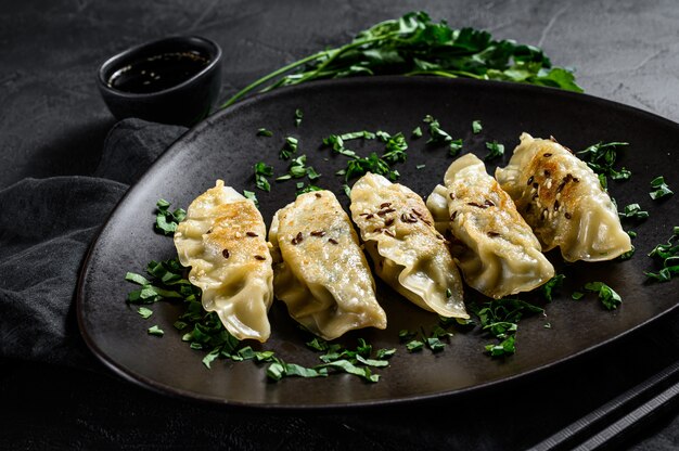 Zdjęcie talerz smażone japońskie pierożki gyoza na rustykalnym czarnym stole. widok z góry.