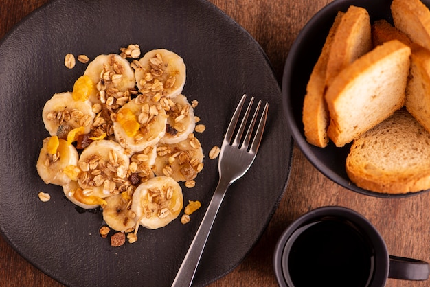 Talerz z pokrojonym bananem i muesli z suszonymi owocami, tostami i filiżanką kawy