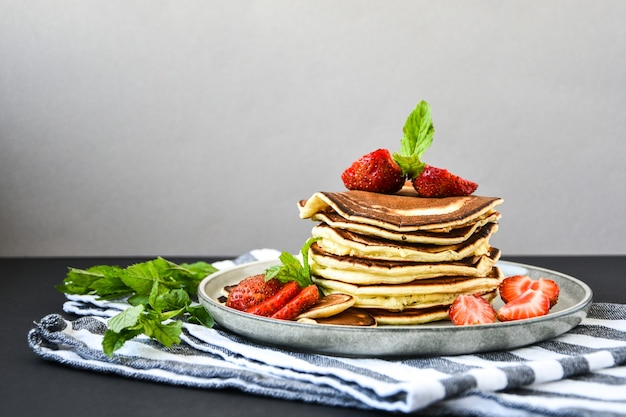 Talerz z tradycyjnych naleśników i Tiny Pancake Cereal z truskawkami i liśćmi mięty na ciemnym tle. Modne jedzenie. Mini naleśniki zbożowe