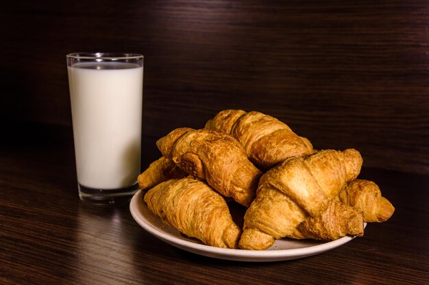 Talerz ze świeżymi rogalikami i szklanką mleka na ciemnym drewnianym stole