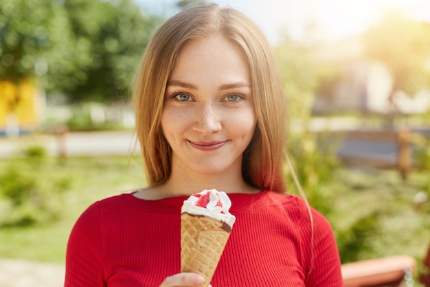 Talia piegowatej zielonookiej dziewczyny z dołeczkami stojącymi z lodami na tle zieleni