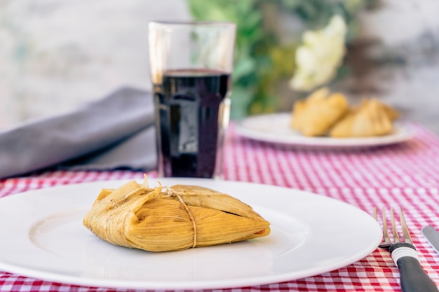 Tamale podawane na białym talerzu na tradycyjnym stole obok kieliszka czerwonego wina. Typowa kanapka lub latynoamerykański posiłek złożony z mąki kukurydzianej i mięsa. Tradycyjne andyjskie jedzenie. Tradycyjna koncepcja żywności