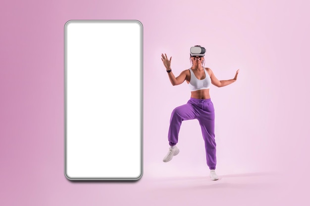 Taniec porusza się w metaverse Młoda kobieta tańczy w słuchawkach wirtualnej rzeczywistości w pobliżu ogromnego smartfona z pustym ekranem