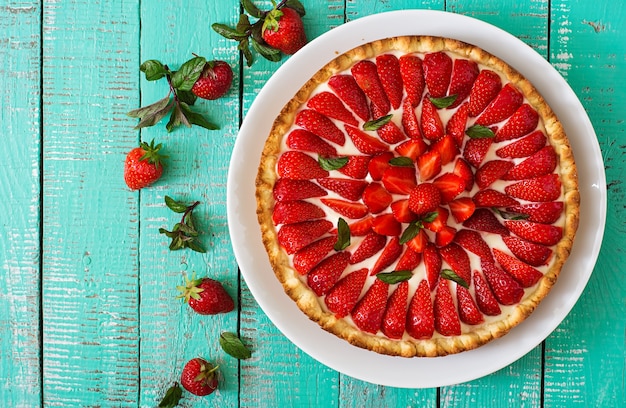 Tarta z truskawkami i bitą śmietaną ozdobiona liśćmi mięty.