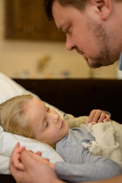 tata głaszcze chore dziecko patrzy z troską z czułością i miłością trzyma za rękę