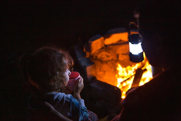 Tata i córka siedzą w nocy przy ognisku na świeżym powietrzu latem na łonie natury Rodzinny wyjazd na kemping, spotkania przy ognisku Grill na Dzień Ojca Latarnia kempingowa i namiot