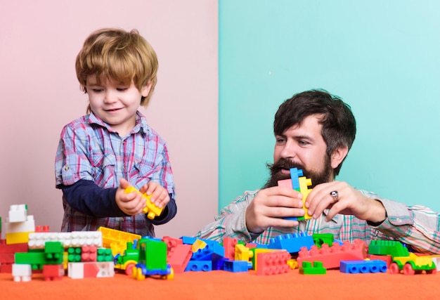 Tata i dziecko budują z plastikowych klocków. Przydatna zabawka. Rozwój i wychowanie dziecka. Gra ojca syna. Ojciec i syn tworzą z klocków kolorowe konstrukcje. Brodaty ojciec i chłopiec bawią się razem.
