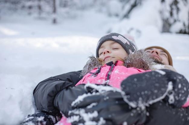 Tata i mała dziewczynka leżąc na śniegu w winter park