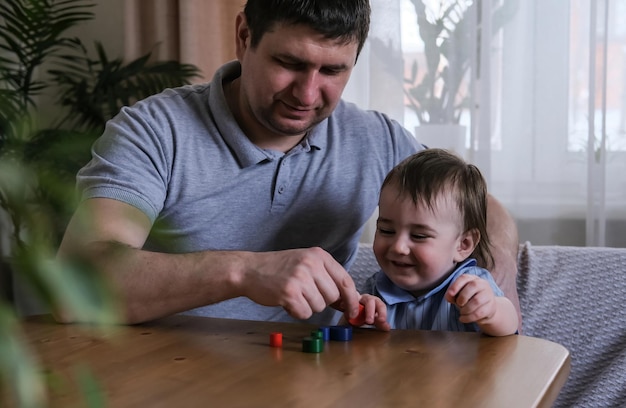 Tata i roczny syn bawią się drewnianymi figurkami w domu Rozwijanie zdolności motorycznych