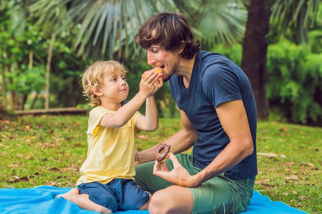 Tata i syn jedzą pączka w parku. Szkodliwe odżywianie w rodzinie.