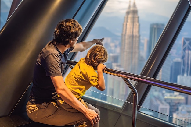 Tata i syn patrzą na panoramę miasta Kuala Lumpur Panoramiczny widok na panoramę miasta Kuala Lumpur wieczorem o zachodzie słońca budynek drapaczy chmur w Malezji Podróżowanie z koncepcją dzieci