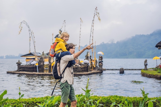 Tata i syn w tle Pura Ulun Danu Bratan na Bali. Świątynia hinduska otoczona kwiatami nad jeziorem Bratan, Bali. Główna świątynia wody Shivaite na Bali, Indonezja. Świątynia hinduska. Podróżowanie z dzieckiem