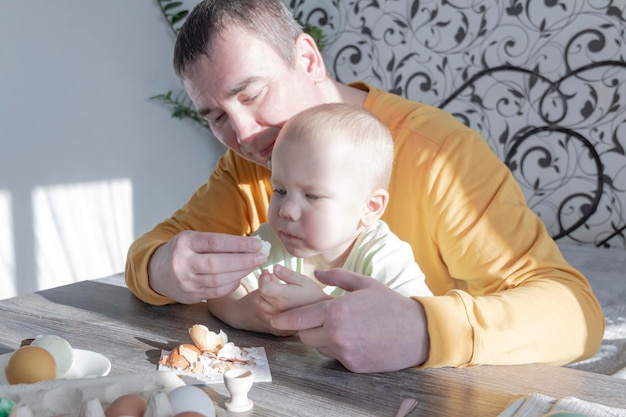 Zdjęcie tata świętuje wielkanoc z małym synkiem biją jajka, jedzą jajka i jedzą śniadanie tata uczy dziecko