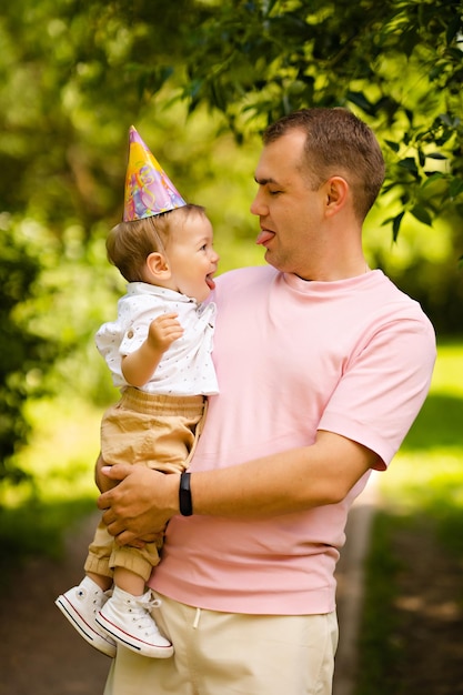 Zdjęcie tata trzymający w ramionach małego synka pokazujący sobie języki, na głowie świąteczną czapkę