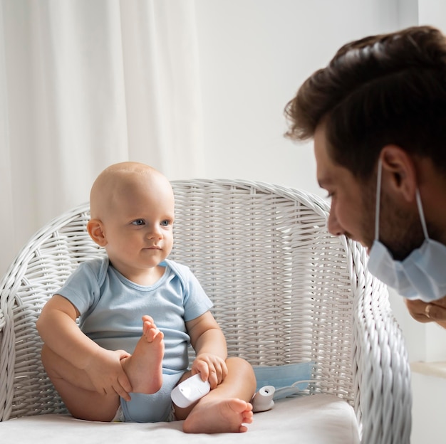 Zdjęcie tata z maską medyczną bawi się z dzieckiem w domu podczas kwarantanny