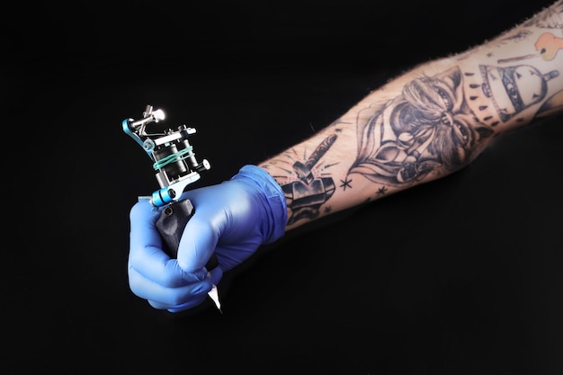 Tattooist ręka w niebieskiej rękawiczce z maszyną do tatuażu na czarnym tle